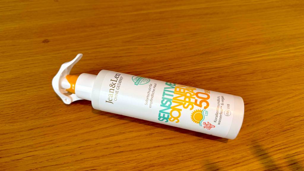 Eine getestete umweltfreundliche Sonnencreme in der weißen Sprühflasche liegt auf einer Holzoberfläche.