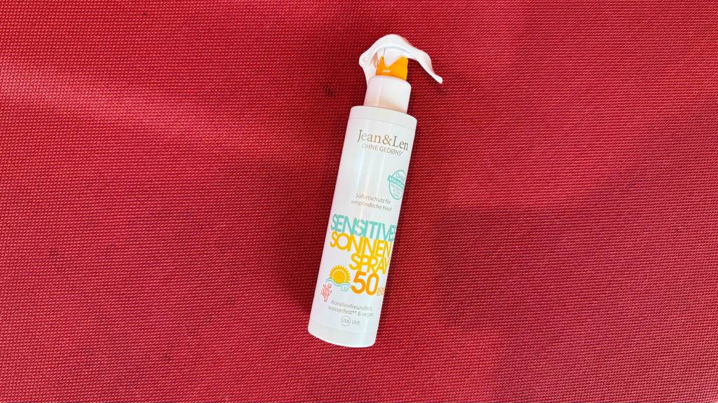 Umweltfreundliche Sonnencremes im Test: Eine weiße Sprühflasche liegt auf einem roten Stoff.