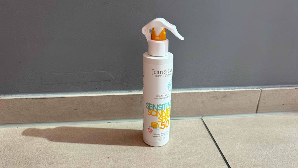 Im Test: Eine umweltfreundliche Sonnencreme in der weißen Sprühflasche steht vor einer grauen Wand.