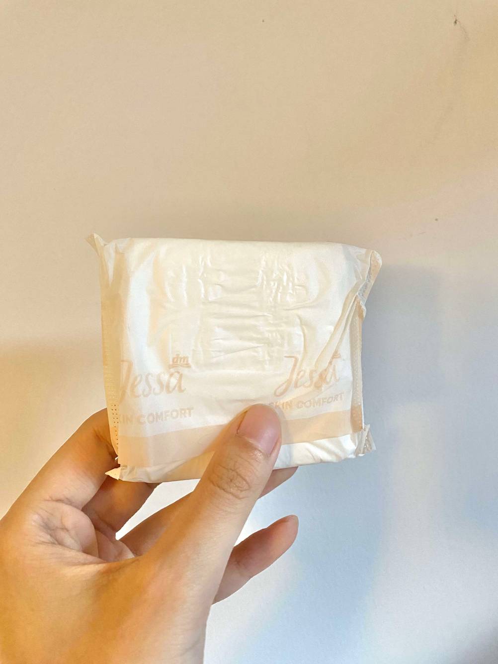 Im Test: Eine Hand hält eine einzeln verpackte Damenbinde vor eine helle Wand.