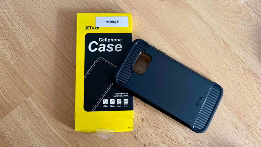 Die getestete Samsung-Galaxy-S7-Hülle in Schwarz liegt auf ihrer schwarz-gelben Verpackung auf einer Holzoberfläche.