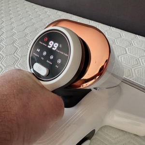 Das Display des Jigoo J300 zeigt 99% an, während eine Hand mit ihm über eine Matratze saugt