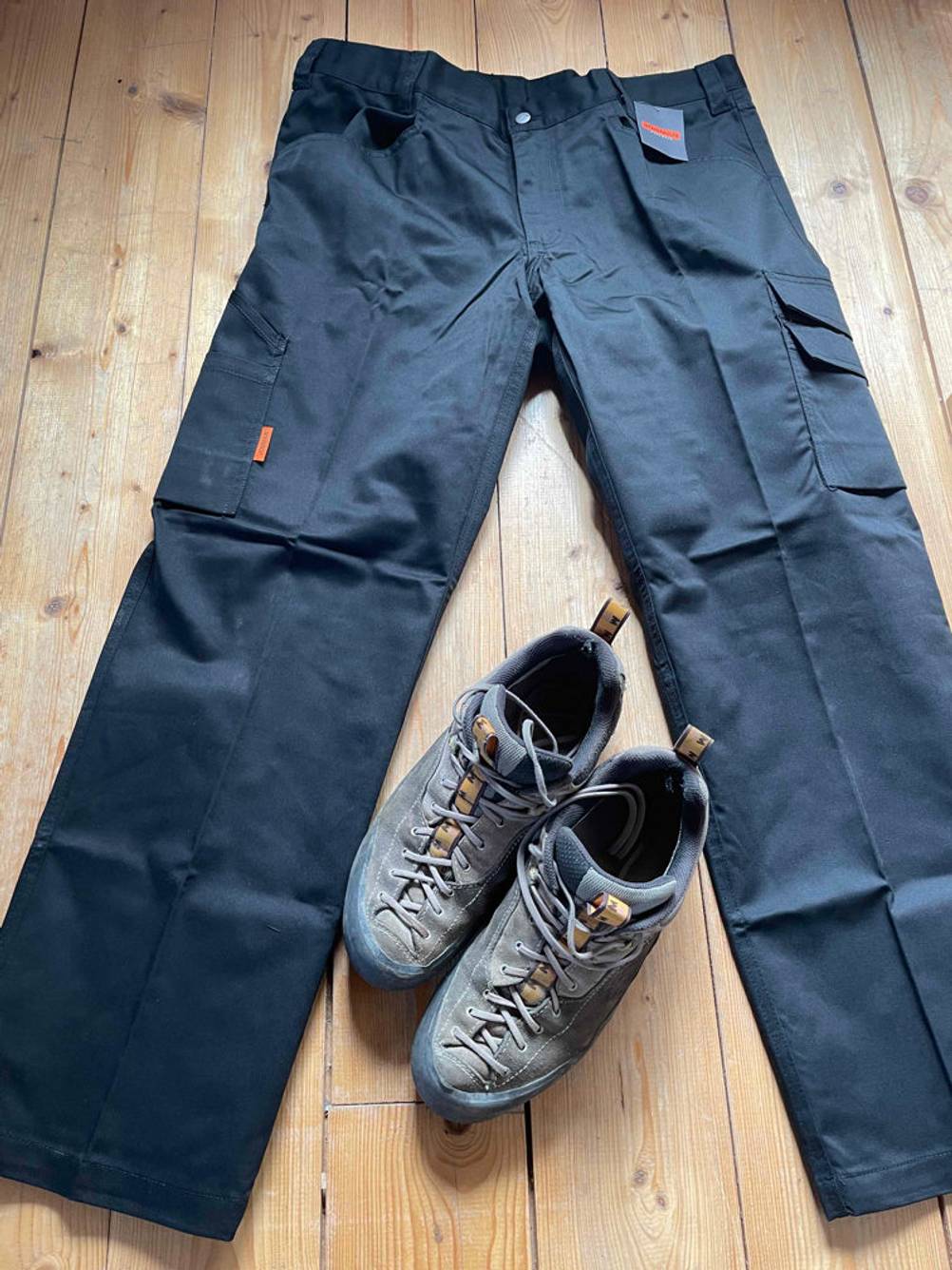 Im Test: Eine Arbeitshose liegt auf einem Holzboden, zwischen den Beinen steht ein Paar Schuhe.