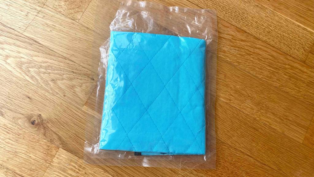 Getestet: Detailansicht des Materials einer Kühlmatte für die Katze, die in einer Plastikverpackung auf einem Holzboden liegt.