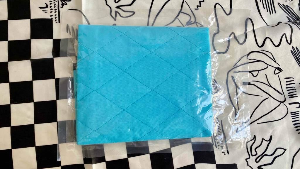 Eine verpackte Kühlmatte für die Katze liegt zum testen auf einem schwarz-weißen Schachbrettmuster-Untergrund.