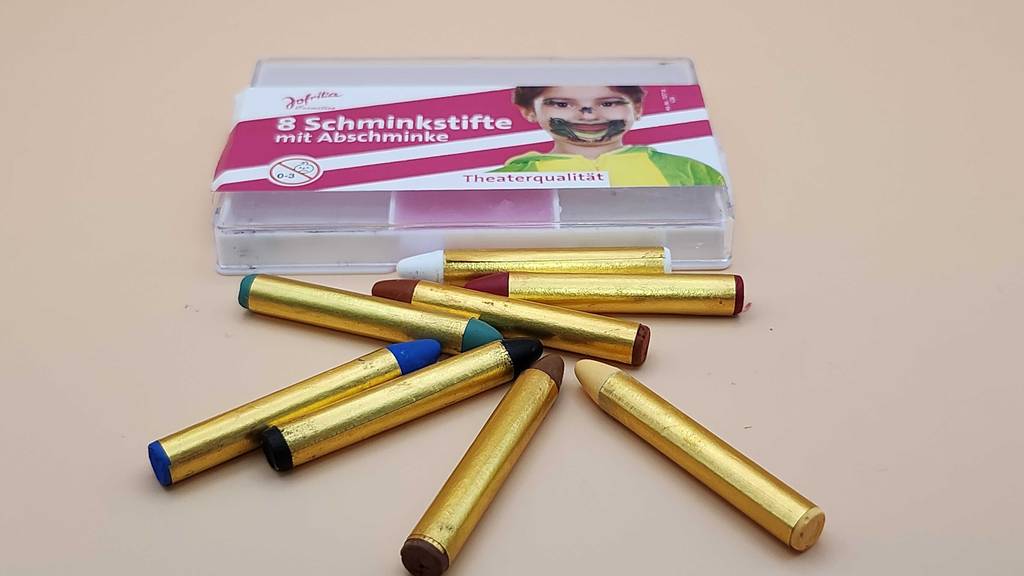 Mehrere farbige Stifte liegen vor einer Packung mit Kinderschminke im Test.