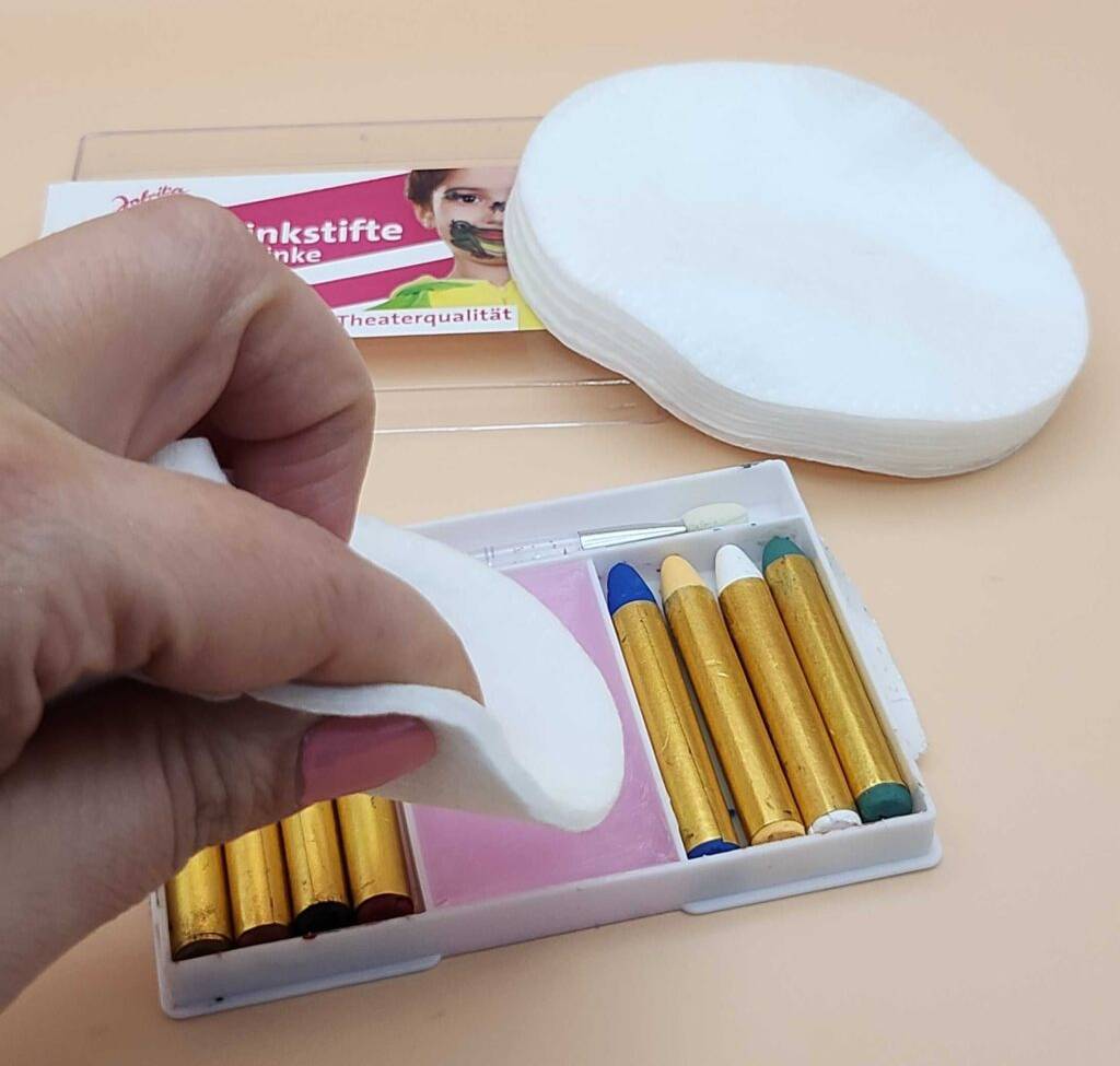 Getestete Kinderschminke: Eine Hand hält einen weißen Schwamm über einer Schminkpackung.
