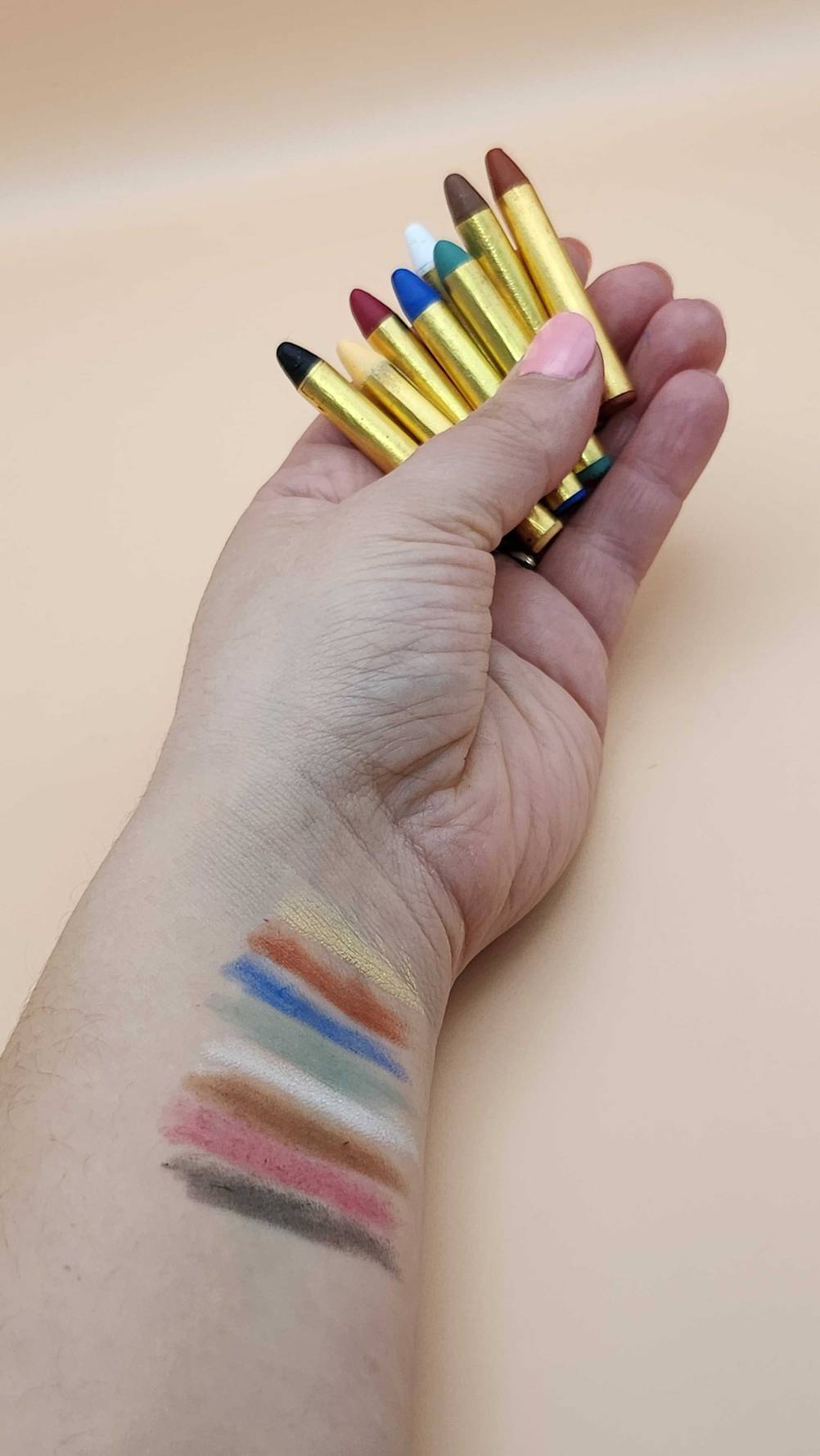 Getestete Kinderschminke in Stiftform: Auf einem Handgelenk sind die Farben gemalt. Schminkstifte liegen in der Hand.