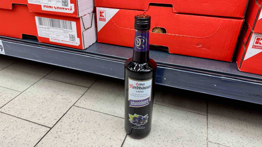Vor einem Regal steht eine Flasche des getesteten Johannisbeerlikörs auf dem Boden.