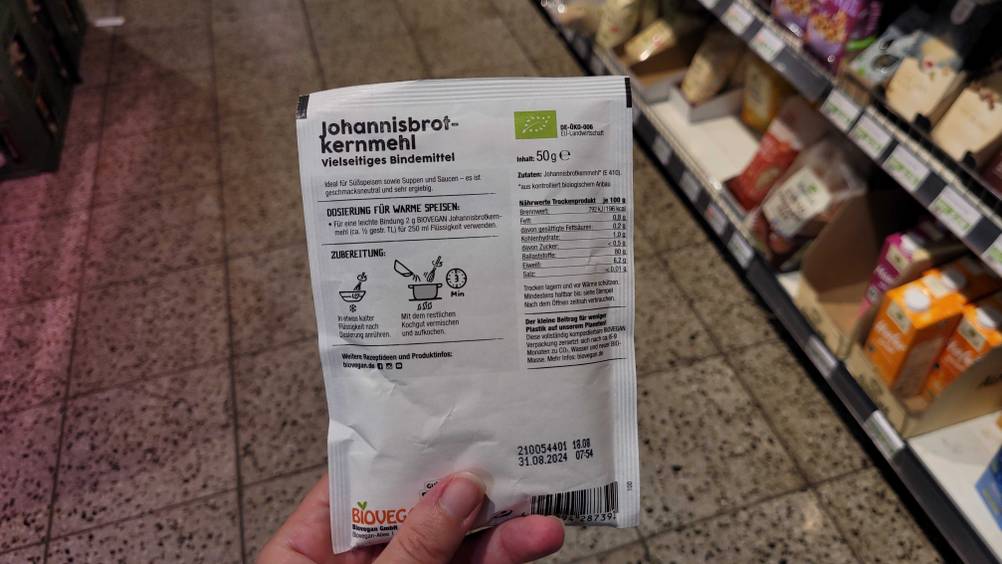 Johannisbrotkernmehl getestet: Rückseite der Verpackung von einer Hand gehalten.