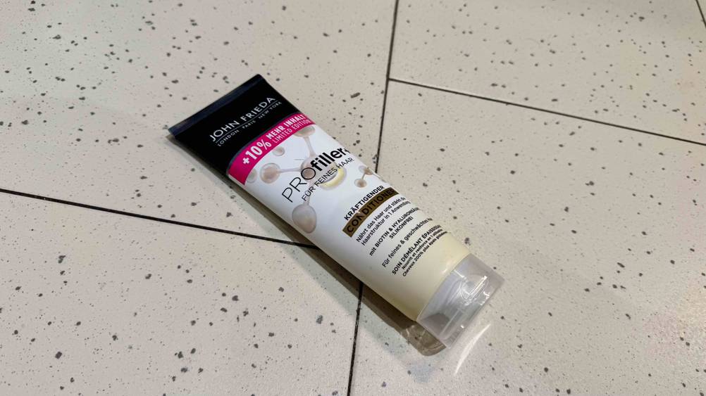 Eine Tube des getesteten John-Frieda-Conditioners liegt horizontal auf einem hellen Fließenboben.