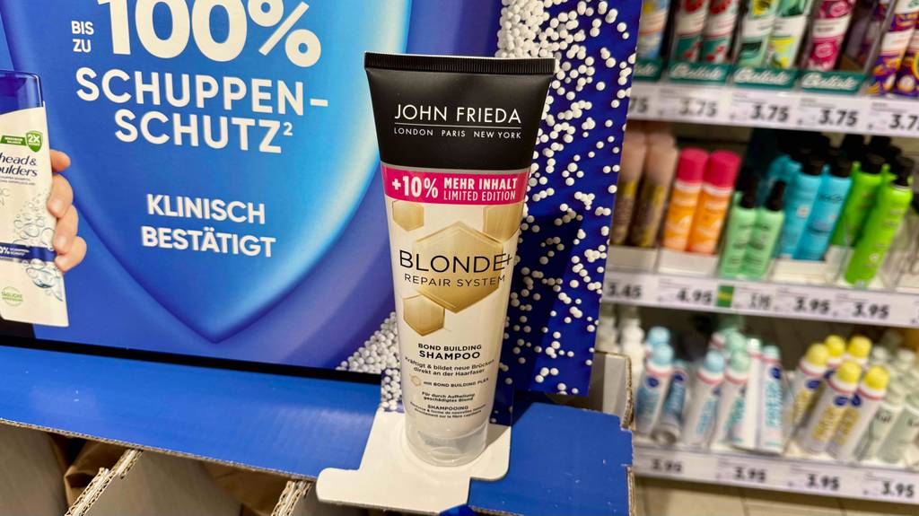 Im Test: Shampoos für blondes Haar, das in einer Tube vor einem Regal mit Kosmetikartikeln steht.
