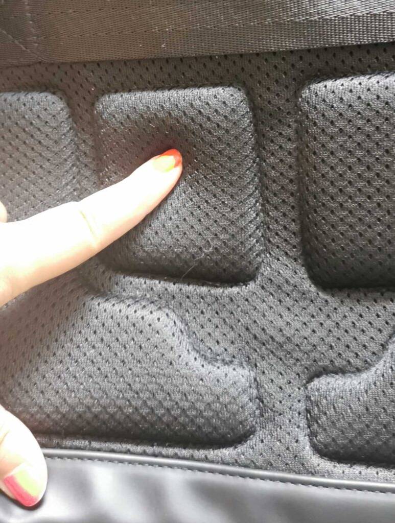 Ein Damenfinger drückt auf die Rückenpolsterung eines grauen, getesteten Handgepäck-Rucksacks.