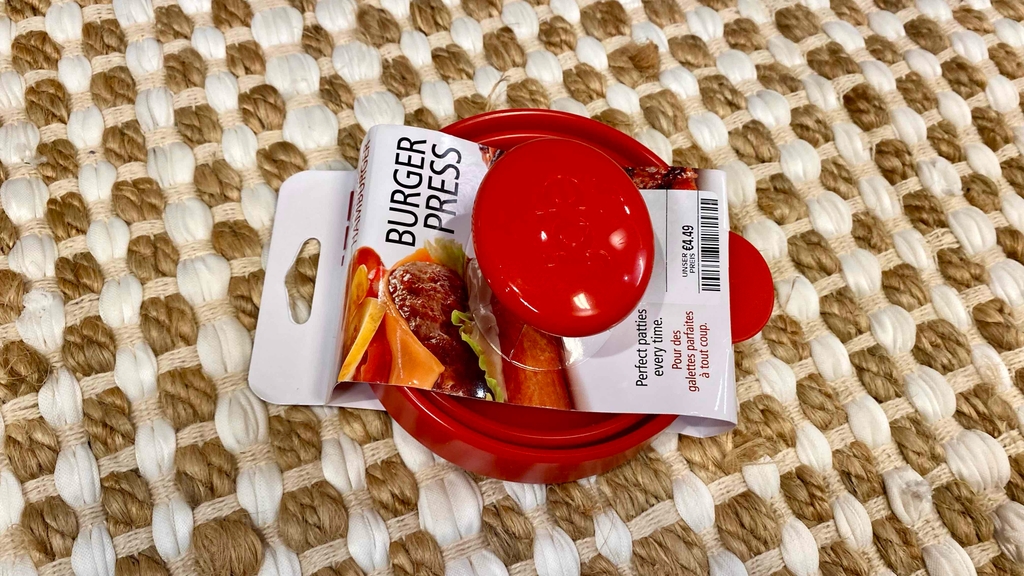 Burgerpressen-Test: Ein rotes Modell inklusive Verpackung liegt auf einem Gewebe.