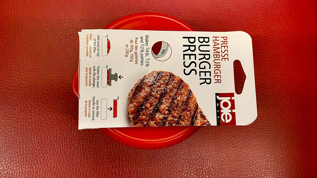 Burgerpressen-Test: Eine rote Handpresse liegt inklusive weißem Verpackungskarton auf einer roten Fläche.