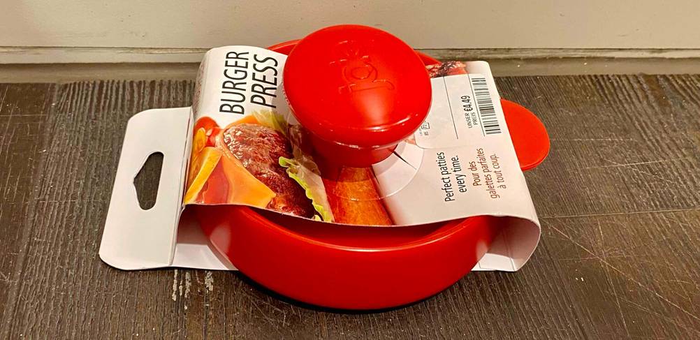 Burgerpressen im Test: Ansicht auf die Höhe des Randes einer roten Lebensmittelpresse, die in ihrem Verkaufskarton auf einer Holzoberfläche liegt.