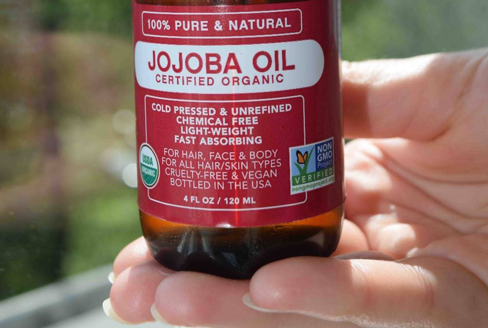 Nahaufnahme des Labels auf der Vorderseite einer Flasche des getesteten Jojobaöls von einer Hand gehalten.