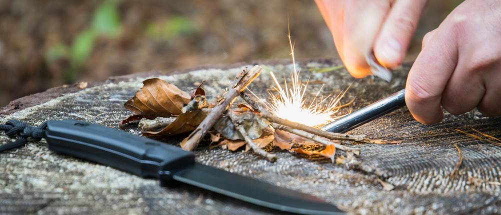Joker-Messer im Test: Messer liegt auf Holzstamm; Hände lassen Funken sprühen, versuchen Feuer zu machen.