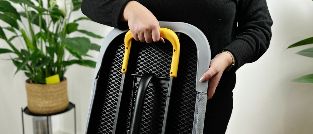 Eine Person hält das zusammengeklappte Joseph-Joseph-Ltd.-Bügelbrett am praktischen Tragebügel. 