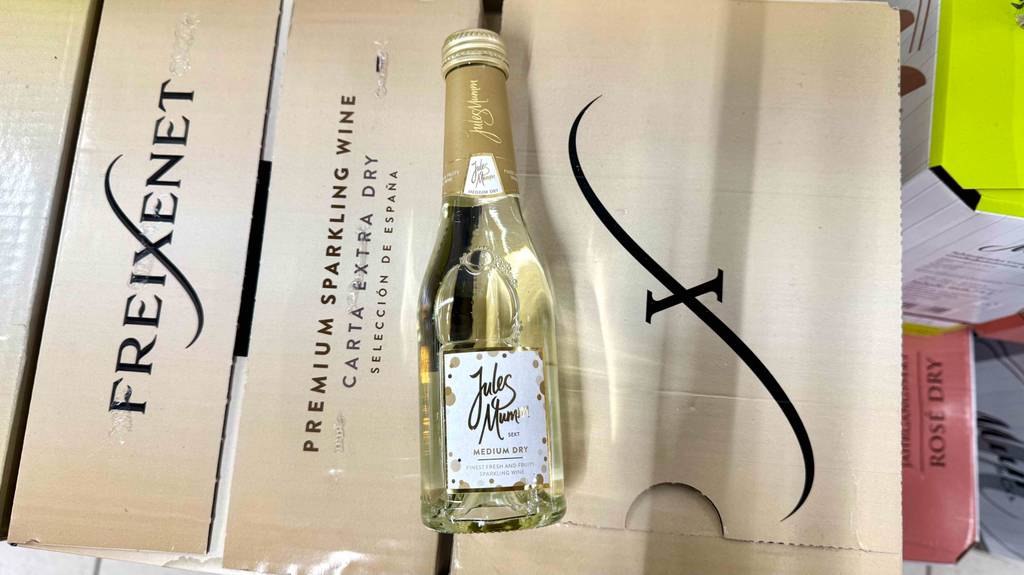 Eine Portionsflasche mit halbtrockenem Sekt im Test liegt auf einem Weinkarton.