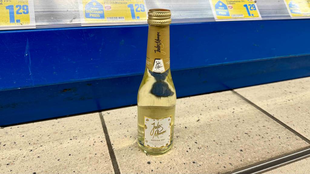 Eine Portionsflasche mit getestetem halbtrockenem Sekt steht vor einem Verkaufsregal.