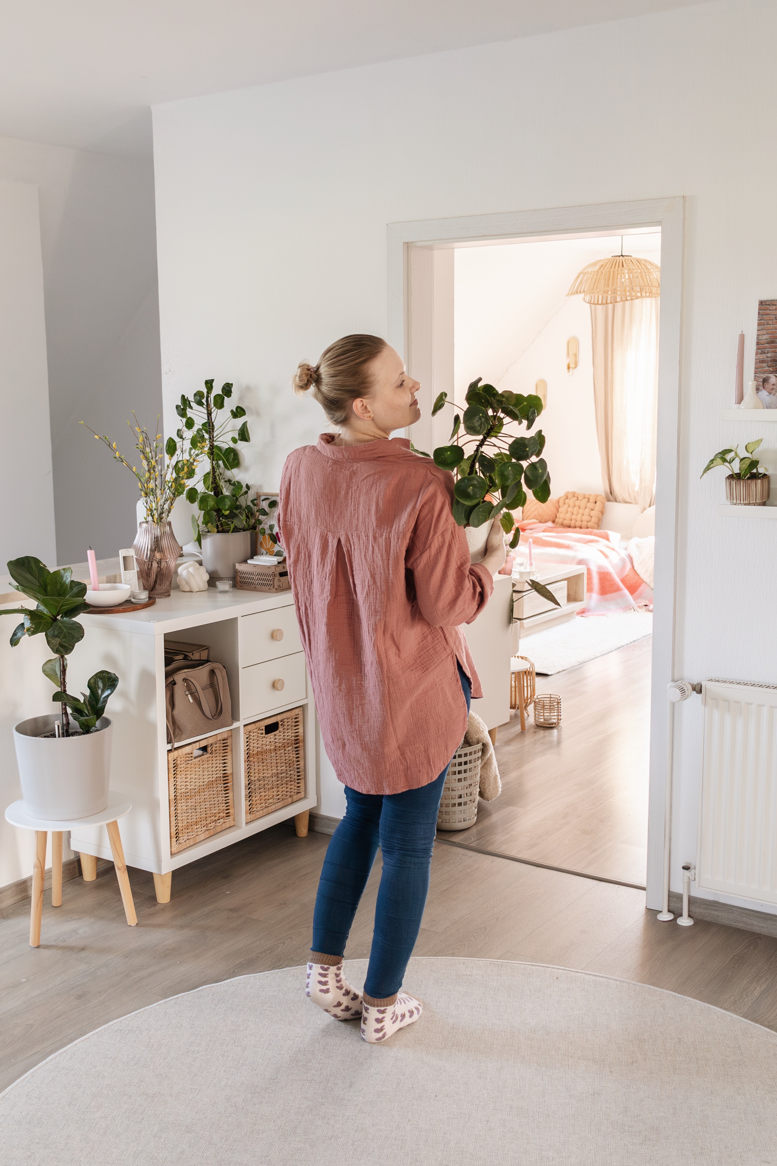 Vergleich.org-Expertin Julia Bittner steht im Wohnzimmer und hält eine Topfpflanze in der Hand. Sie dreht der Kamera den Rücken zu, das Gesicht ist im Profil zu sehen