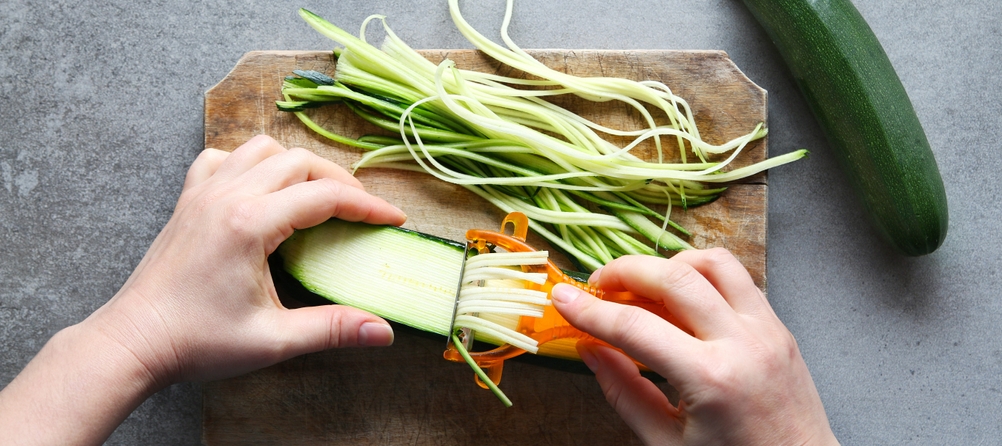 Ein Pendelschäler mit Julienne-Funktion wird bei einer Zucchini eingesetzt.