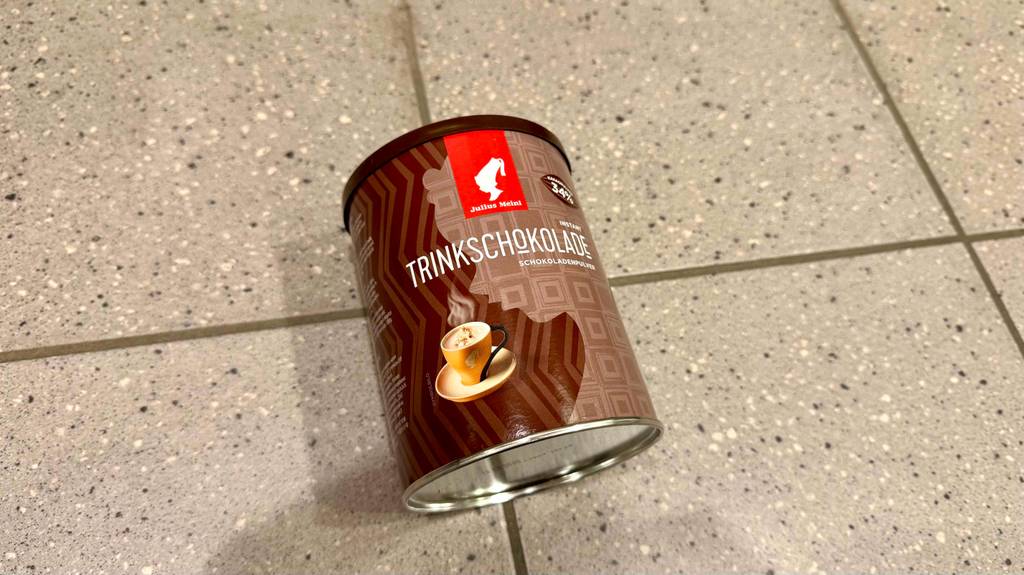 Eine wiederverschließbare Dose mit getesteter Trinkschokolade in Pulverform liegt auf einem Fliesenbelag.