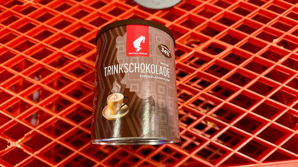 Im Test: Trinkschokolade in der wiederverschließbaren Dose liegt auf einem roten Kunststoffgitter.