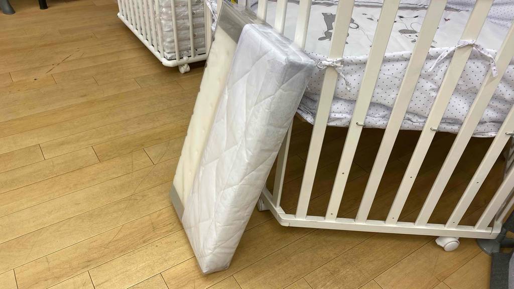 Getestet: Eine Babymatratze lehnt in ihrer durchsichtigen Originalverpackung an einem Kinderbett.