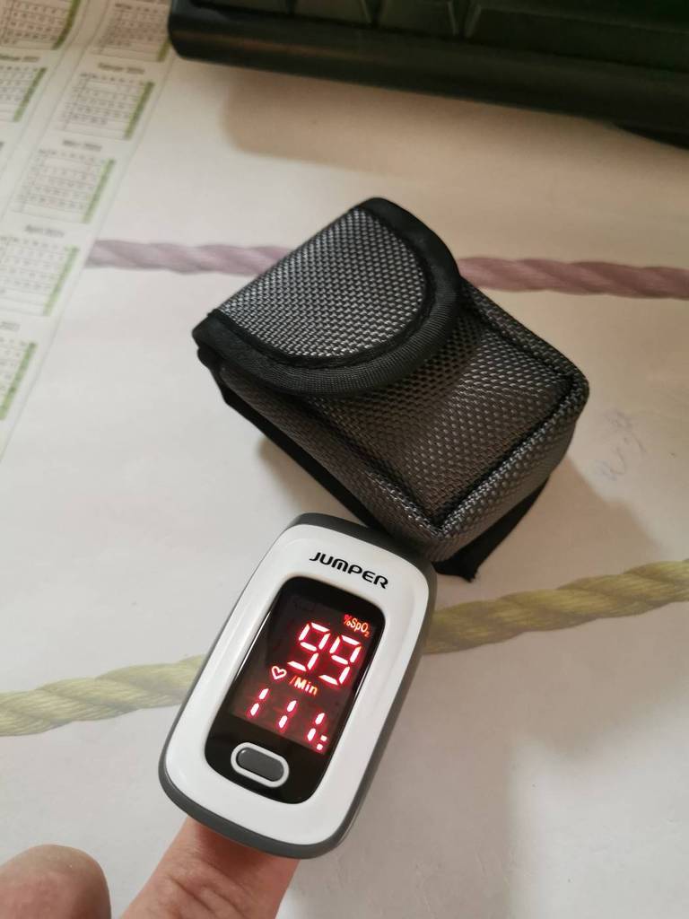 Weiß-schwarzer, messender und getesteter Pulsoximeter von Jumper an einem Zeigefinger neben seiner schwarzen Aufbewahrungstasche.
