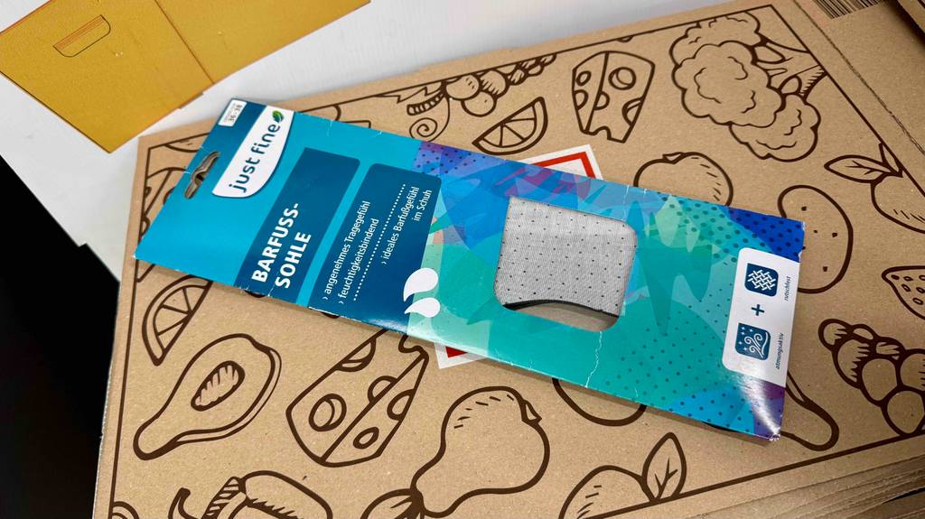 Getestete Barfußsohlen in der blauen Verpackung liegen auf einem braunen Karton.