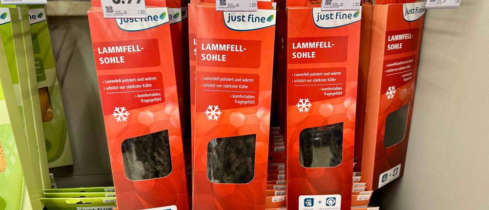 Mehrere Lammfellsohlen im Test befinden sich in roten Verpackungen an einem Verkaufsregal inklusive Preisschildern.