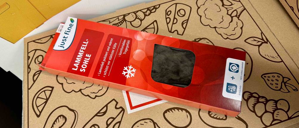 Eine Lammfellsohle im Test liegt in der roten Verpackung auf einem brauenen Karton.