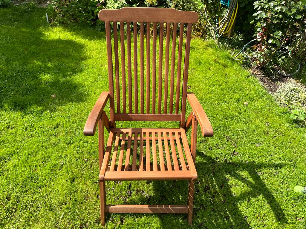 Ein klappbarer Gartenstuhl aus Holz mit Rücken- und Armlehnen steht auf einem grünen Rasen.