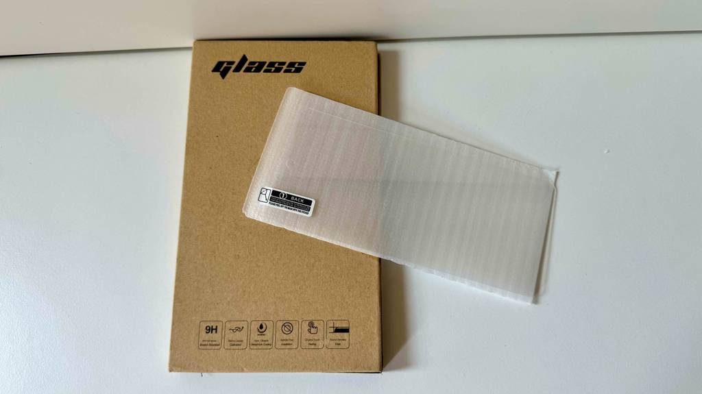 Ein in Schutzfolie verpacktes Samsung Galaxy A51-Panzerglas liegt quer zum Testen auf dem geschlossenen Etui.