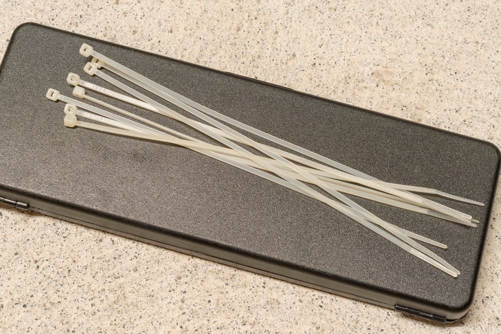 Kabelbinderzange im Test: Ein Case in Anthrazit auf dem einige Kabelbinder in Weiß liegen.