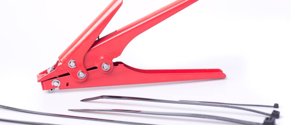 Kabelbinderzange im Test: eine manuelle Zange mit vier schwarzen Kabelbindern auf weißem Grund.