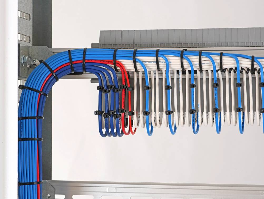 Kabelbinderzange im Test: Eine saubere Kabelführung mit vielen Kabelbindern in Blau, Rot und Schwarz auf neutralem Hintergrund.