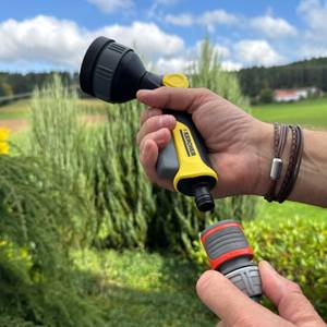 Eine Hand steckt die Kärcher-Multifunktions-Spritzpistole Plus in einen Schlauch