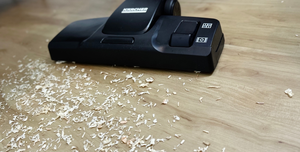 Die Bodendüse des Kärcher VC 3 liegt auf einem Holzboden, umgeben von Holzspänen. Das Gerät befindet sich im Betrieb.