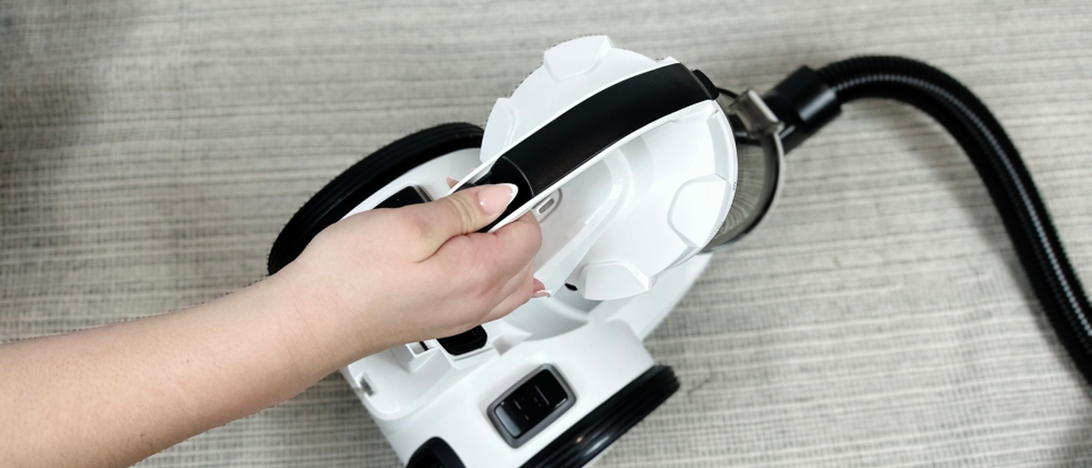 Der Kärcher VC 3 wird von oben mit einer Hand am Griff getragen. Das Gerät liegt auf einem Teppichboden.