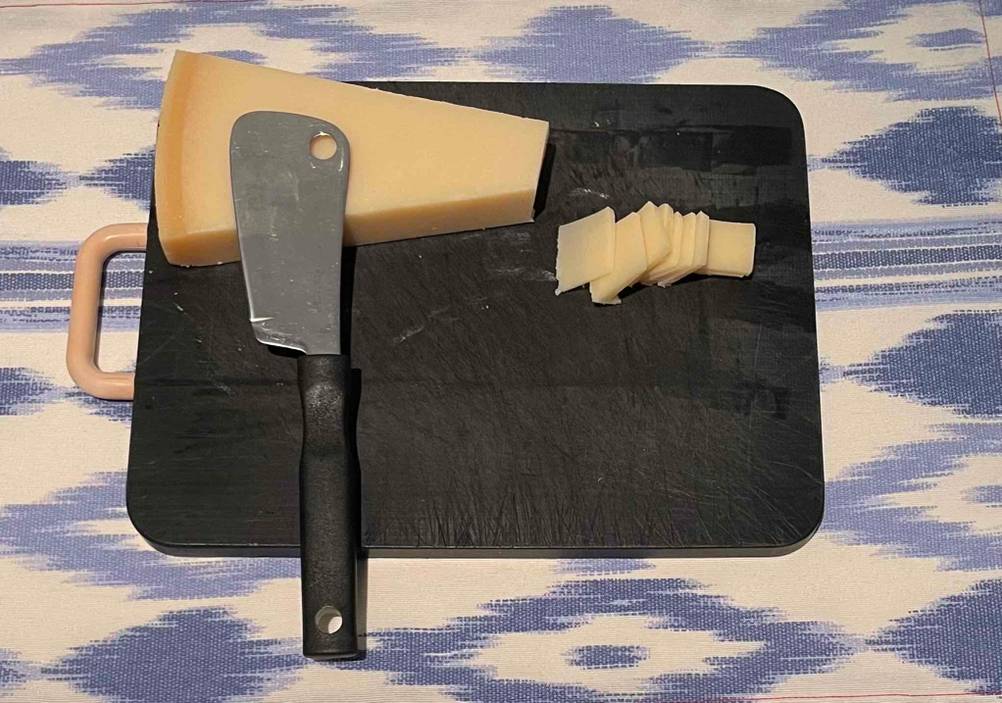 Ein Käsemesser im Test befindet sich auf einem schwarzen Brettchen, auf dem in Scheiben geschnittener Käse liegt.