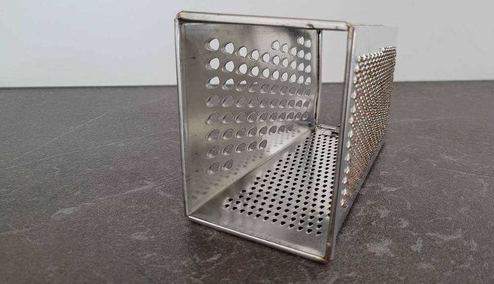 Innenansicht einer getesteten Käsereibe auf einer dunklen Arbeitsfläche.
