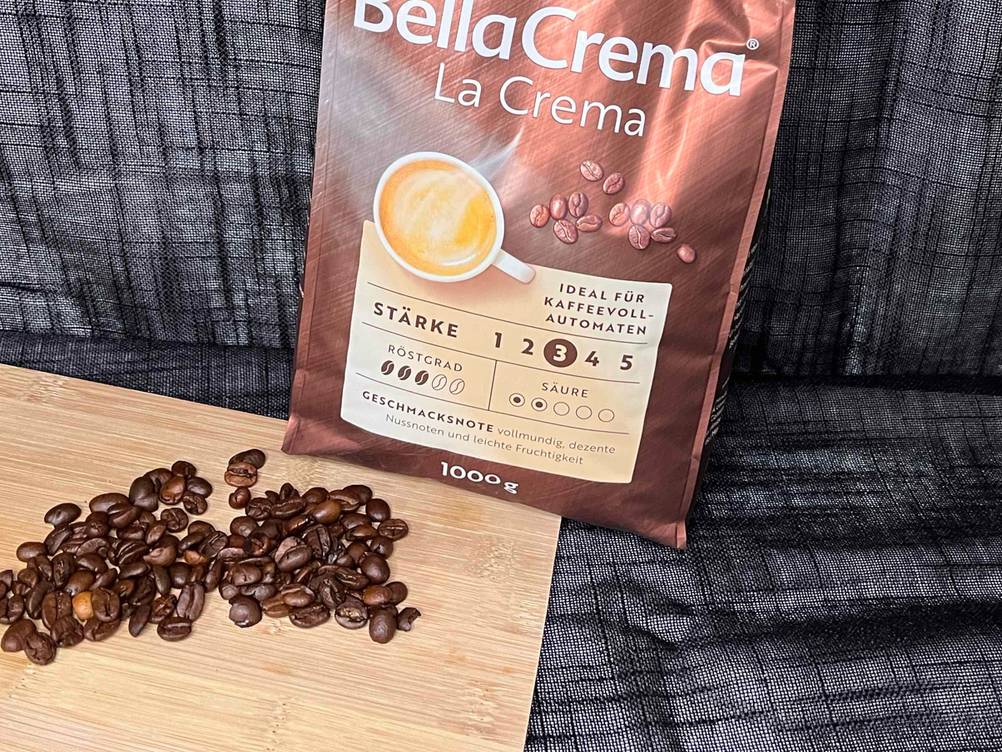 Vor einer Packung der getesteten Kaffeebohnen liegen auf einem Holzbrett eine Handvoll Bohnen.