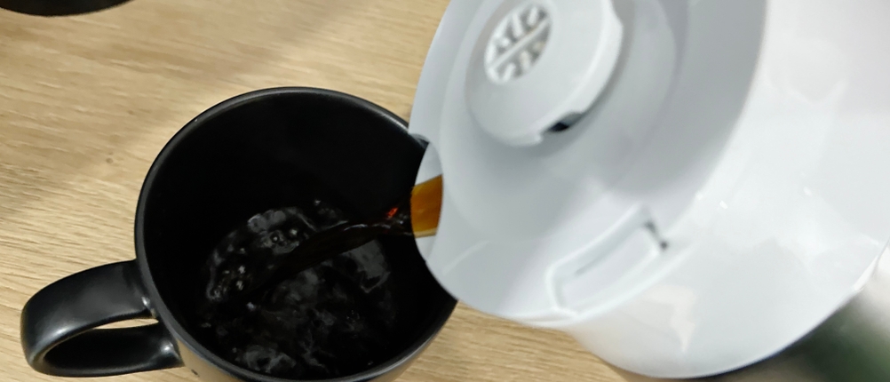 Frisch gebrühter Kaffee wird aus der Thermoskanne der Melitta Look V Perfection in eine schwarze Tasse gegossen. Der Ausguss ist geöffnet.