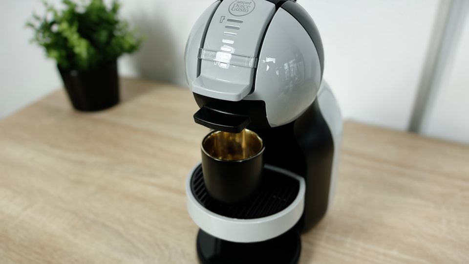 Die Krups Nescafé Dolce Gusto Mini Me KP120H steht auf einem Holztisch. Eine schwarze Tasse steht unter dem Kaffeeauslauf.