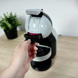 Das Kapselfach der Krups Nescafé Dolce Gusto Mini Me KP120H wird geöffnet. Eine Kapsel wird von einer Hand eingeschoben.