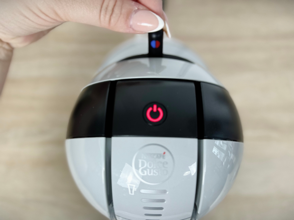 Eine Hand berührt den Power-Button der Krups Mini Me KP120H. Die Taste auf der Oberseite leuchtet rot.