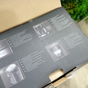 Die Verpackung der Krups KM8328 zeigt Produktmerkmale in mehreren Sprachen. Zu sehen sind Fotos und Funktionshinweise der Kaffeemaschine mit Mahlwerk.